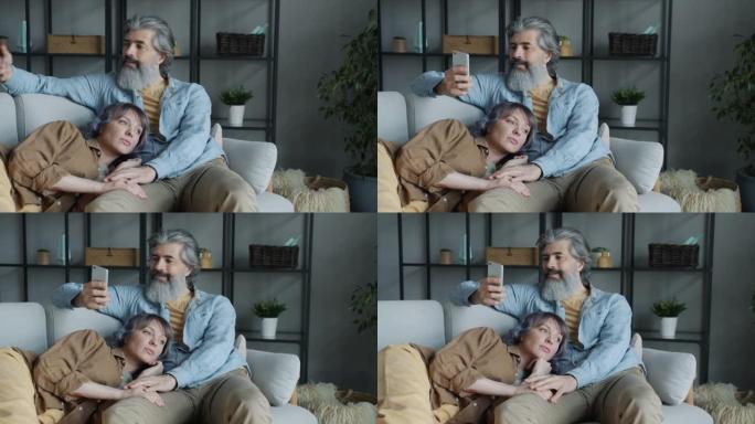 成熟的男人使用智能手机，拥抱美丽的妻子躺在家里的膝盖上