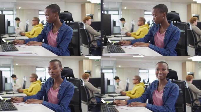 非裔美国妇女坐在办公桌前工作，在办公室对着镜头转身微笑