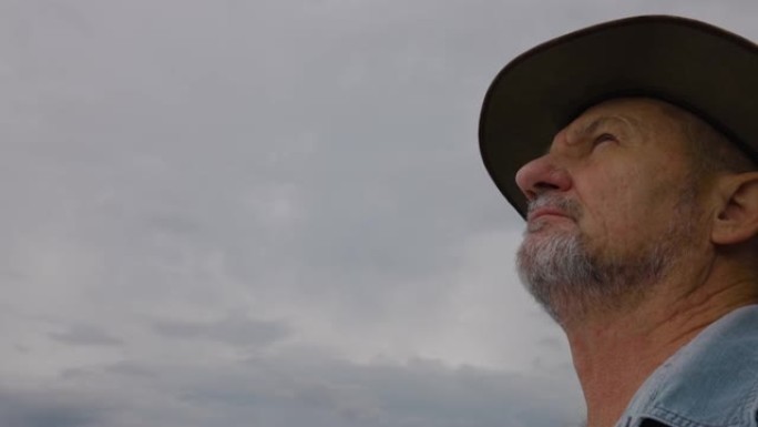 气候变化。一位戴着帽子的老农民的特写肖像看着天空等待下雨以缓解干旱