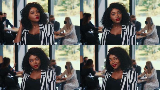年轻的20多岁美丽的黑人女商人的肖像看着相机触摸卷曲的头发在轻办公室慢动作。