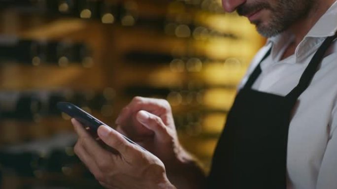 现代农民或酿酒师正在使用智能手机上的酒庄在线商务应用程序来检查客户服务并在酒窖中销售他的葡萄酒生产的