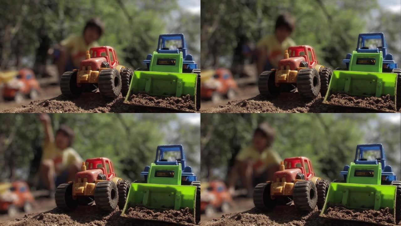 塑料拖拉机玩具和塑料挖掘机玩具或玩具推土机和一个模糊的孩子在背景中玩耍。特写。