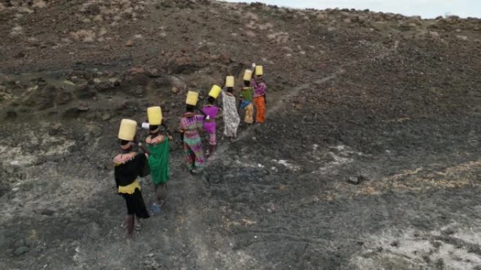 气候变化，干旱，水危机。鸟瞰图。非洲妇女从肯尼亚图尔卡纳地区的火山泉水中收集塑料容器中的水后回家