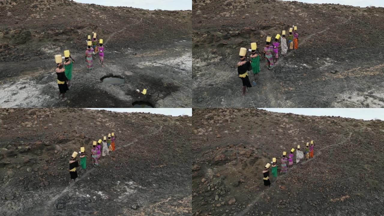 气候变化，干旱，水危机。鸟瞰图。非洲妇女从肯尼亚图尔卡纳地区的火山泉水中收集塑料容器中的水后回家