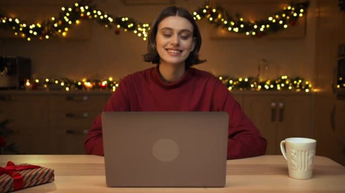 一个年轻漂亮的女人正在她的笔记本电脑上视频聊天，坐在桌子旁喝杯茶