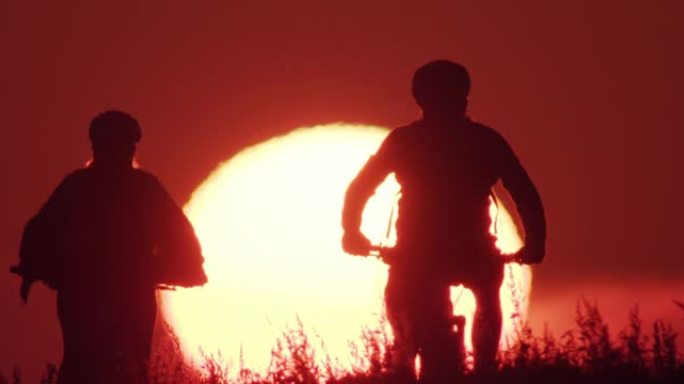两名骑自行车的人在欣赏日落时高五的剪影