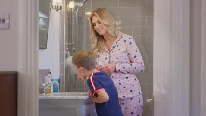 母亲在家里的浴室里用木制牙刷照镜子帮助儿子刷牙