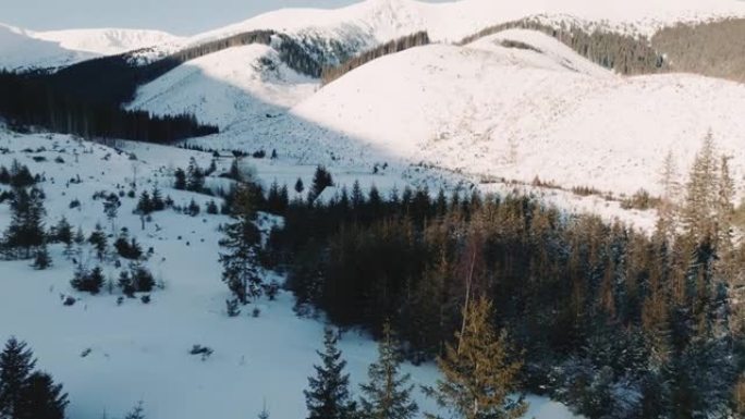 无人机飞越美丽阳光明媚的冬季景观，积雪覆盖的山坡，冰冻的树木，房屋和曲棍球场。