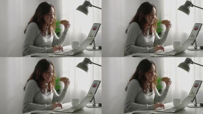 亚洲女商人在笔记本电脑上工作时吃甜甜圈