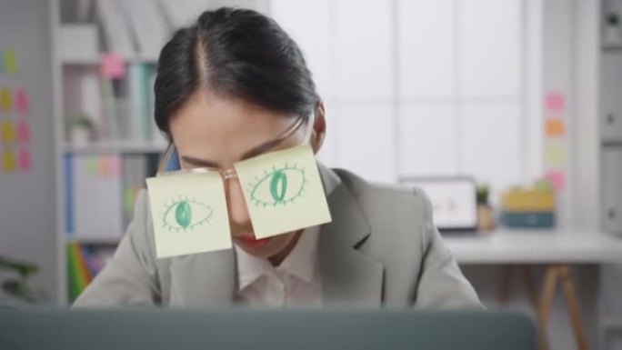 年轻的亚洲女商人坐在办公桌上劳累劳累，睡在办公室的笔记本电脑上。