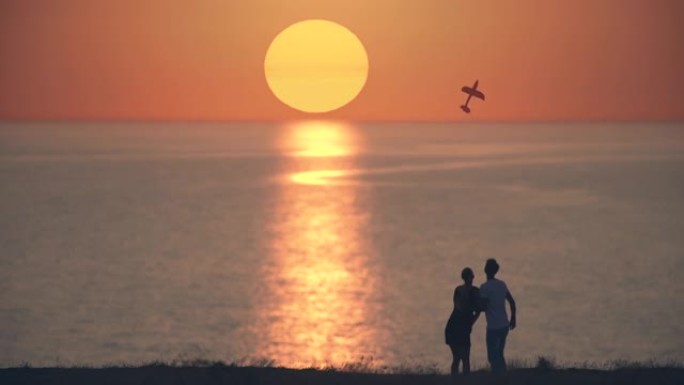 男人和女人把玩具飞机扔在日落背景上。慢动作