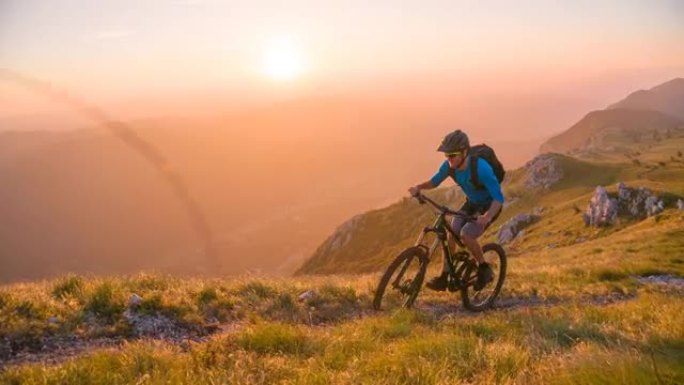 在美丽的晴天，男运动员越野骑自行车上坡，背景是分层的山脉