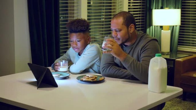 男孩和继父在平板电脑上看电视，吃零食