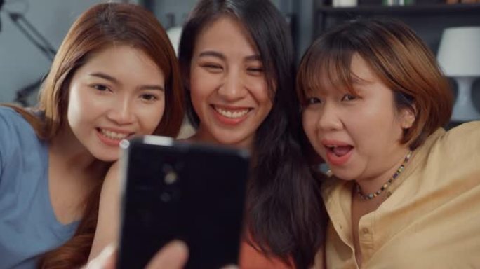 一群年轻的亚洲女性感到快乐的微笑放松在家里的客厅使用智能手机视频通话。开朗的室友女士视频会议与朋友，