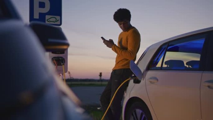 SLO MO年轻人在黄昏时给他的电动汽车充电