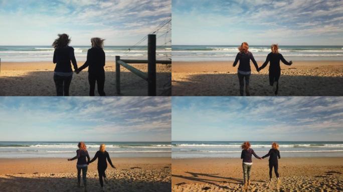 两个女性朋友的慢动作感到自由，在日落时分带着白色沙滩的荒岛海滩上，手拉手奔向蓝色的大海。