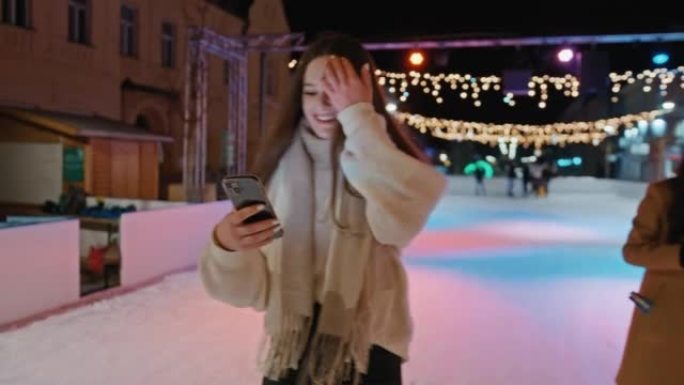 快乐的年轻女子在溜冰场上滑冰时使用手机