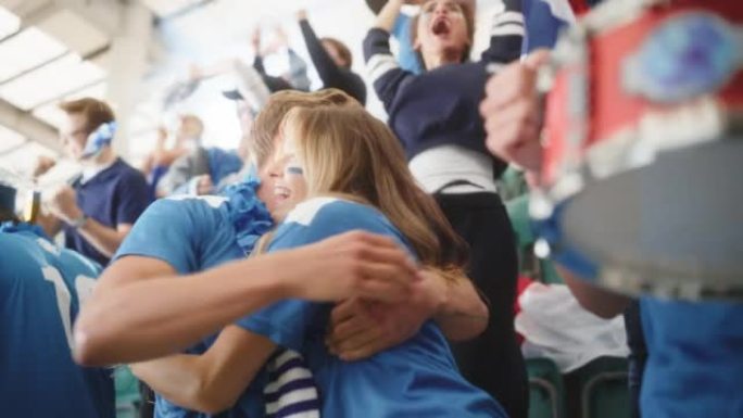 体育馆大事件: 一群球迷为他们的蓝色足球队获胜而欢呼。人们庆祝进球，冠军胜利。可爱的年轻夫妇画着脸欢