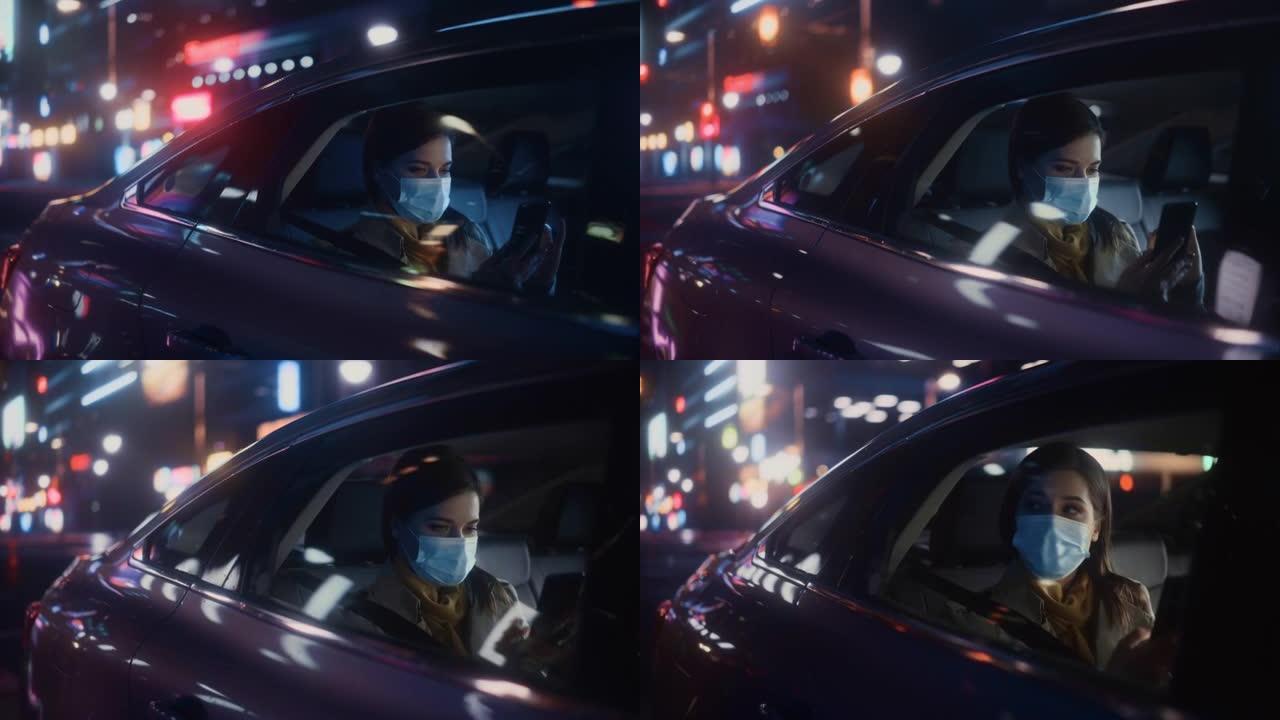 戴着口罩的女性晚上在出租车的后座上通勤回家。美丽的乘客使用智能手机，在城市街道上开着霓虹灯的汽车时看