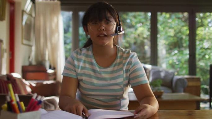 亚洲女孩坐在桌旁戴着耳机进行视频通话