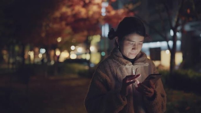 亚洲妇女晚上在公园里用电话散步