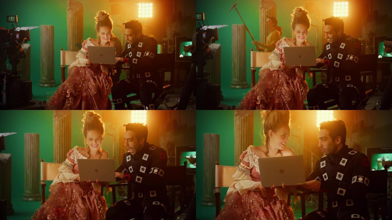 微笑的女演员穿着文艺复兴服装，演员穿着运动捕捉服坐在椅子上，使用笔记本电脑。工作室拍摄高预算电影。论