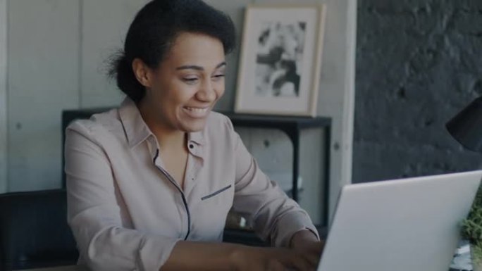 兴奋的年轻女商人表达了与笔记本电脑一起工作的快乐，在现代办公室获得了好消息