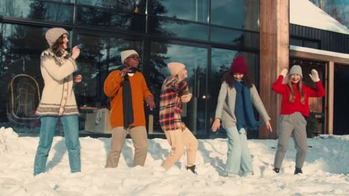 寒假。一群快乐有趣的多民族年轻朋友在阳光明媚的雪屋露台慢动作一起跳舞。