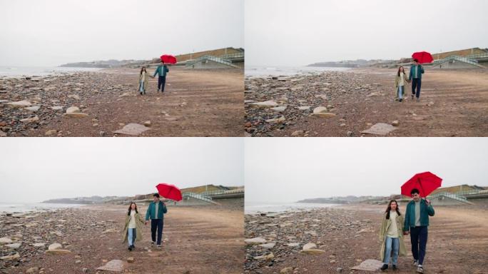 夫妇沿着海滩散步房子伞石头