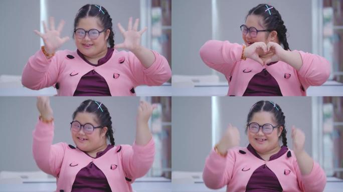 一个15岁的亚洲小女孩戴着眼镜，带着唐氏综合症微笑着站在教室里看着摄像机。残疾的肖像