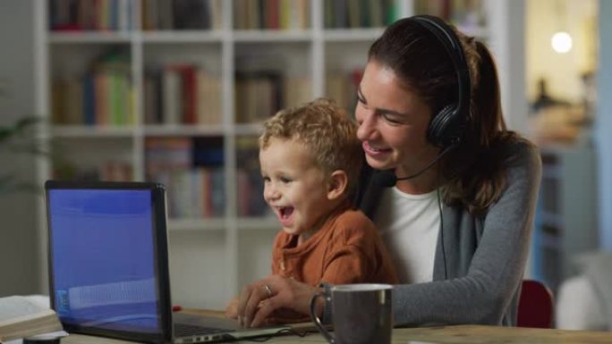 在家工作: 年轻母亲的肖像，她抱着可爱的蹒跚学步的孩子，白天在笔记本电脑上工作。成功的女经理在参加远