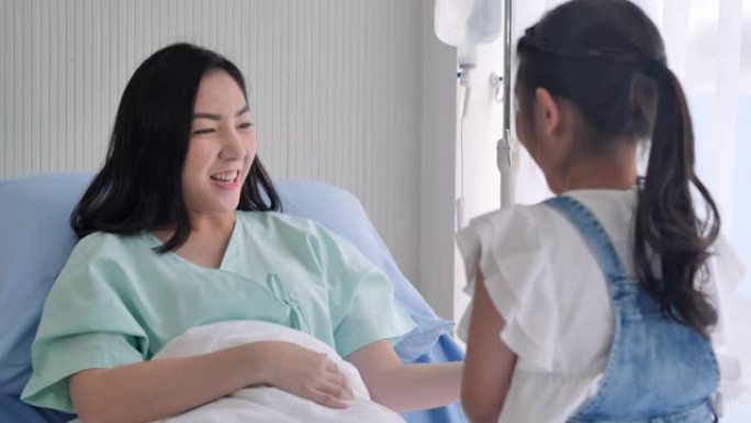 亚洲little女孩抱着泰迪熊，在医院的病床上对母亲嬉戏。单亲家庭