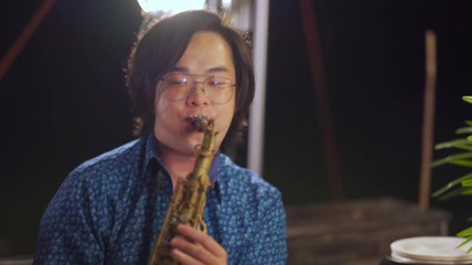 亚洲中国萨克斯风演奏家晚上在花园聚会露营帐篷中与家人和朋友一起演奏萨克斯风