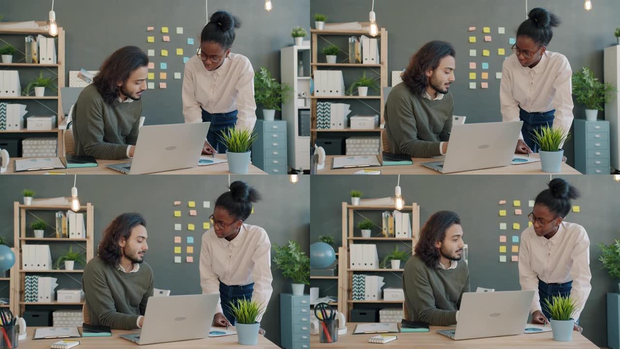 多种族的团队女孩和男孩在工作场所聊天和看文件和笔记本电脑屏幕
