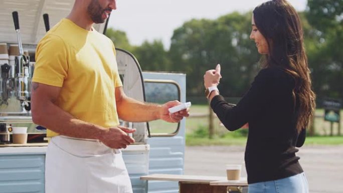 女性客户使用智能手表向移动咖啡货车的女性所有者进行非接触式付款-慢动作拍摄