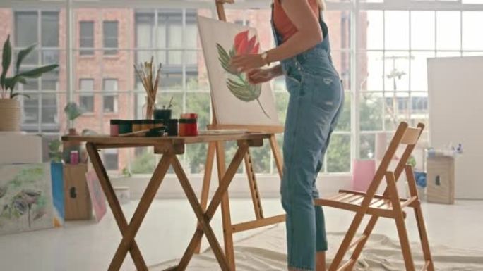 熟练的艺术家在画架上用画笔调色板和纸在画架上单独在工作室里画一朵花。一位富有创造力的女性坐在艺术工作