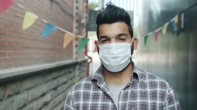 城市户外站立着戴着医用口罩的严肃阿拉伯男子的肖像