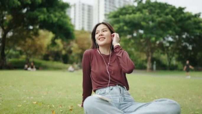 美丽的女孩在绿色公园使用智能手机在耳机中听音乐