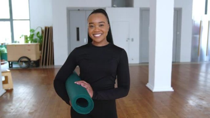 健身工作室里带着瑜伽垫微笑的非洲女人的肖像