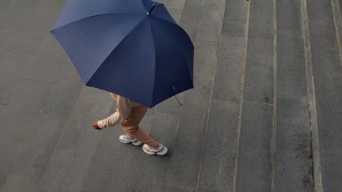 一位年轻的深色皮肤的女商人穿着米色衣服，带着雨伞从商务中心走下楼梯