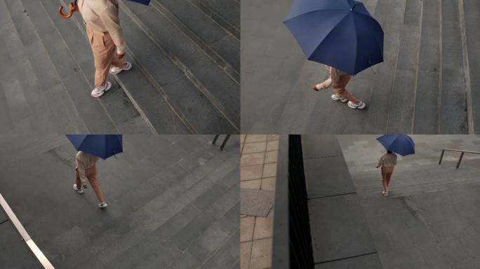 一位年轻的深色皮肤的女商人穿着米色衣服，带着雨伞从商务中心走下楼梯