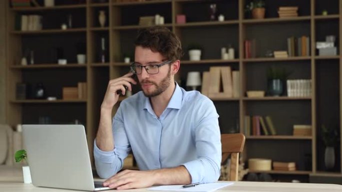 千禧一代商人坐在笔记本电脑上与客户使用电话进行谈判