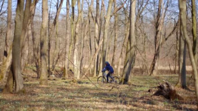 穿着蓝色夹克的男孩在秋天的森林小径上骑自行车