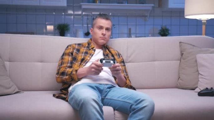 年轻英俊的游戏玩家坐在沙发上，在数字控制台上玩视频游戏的肖像。控制视频游戏操纵杆的反应男性玩家。一个