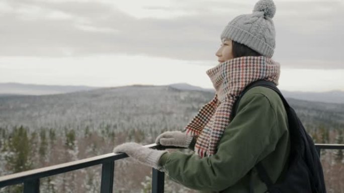 快乐的亚洲女士观看美妙的冬季景观，从户外的观察地点看森林和山脉