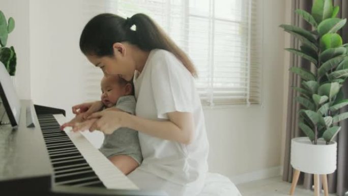 单身母亲抱着刚出生的男婴手在家里弹钢琴。她教她可爱的孩子演奏古典乐器。