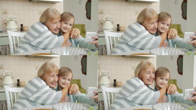 现代小女孩与爱的祖母自拍，用智能手机摆姿势拥抱相机