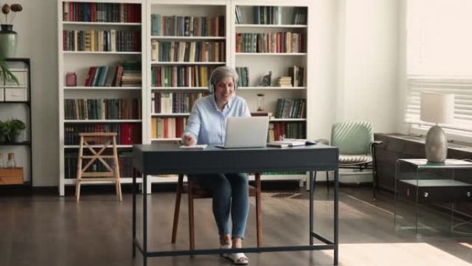 年长的女人坐在桌子上，用笔记本电脑进行视频电子学习