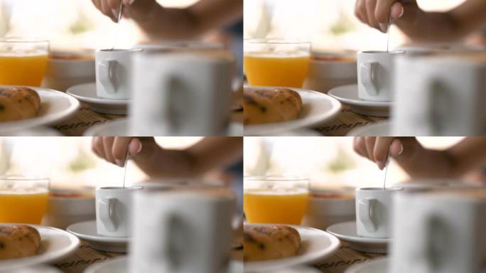 一个年轻女子的真实特写镜头是在白瓷杯中混合咖啡中的糖，同时早上在咖啡馆或酒吧享用新鲜健康的糖尿病早餐