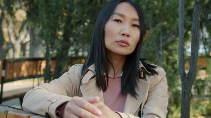 严肃的年轻亚洲女商人的肖像看着坐在城市公园外面的相机
